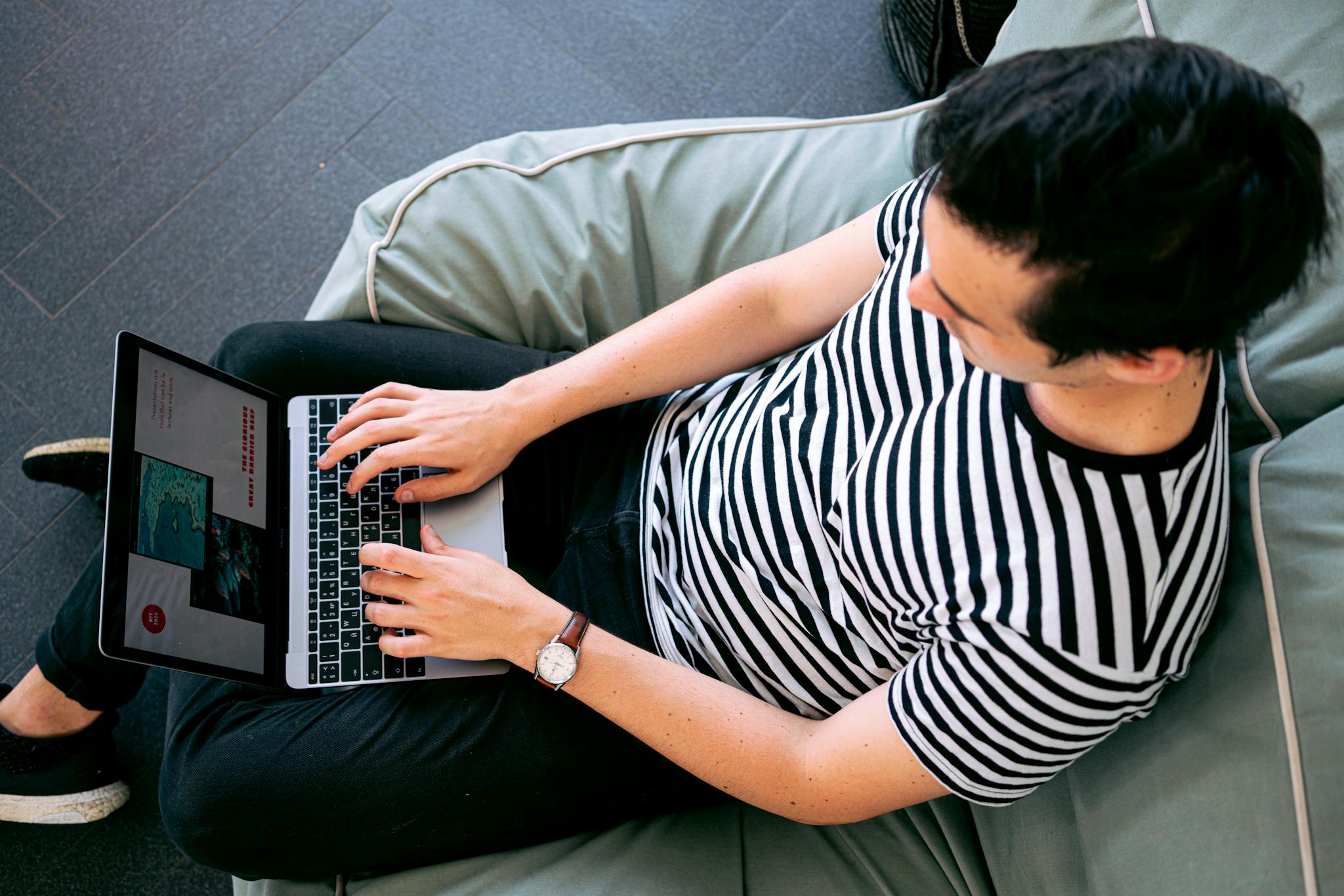 Alps Edition A man in a striped shirt using a laptop on a bean bag, embodying relaxed productivity.