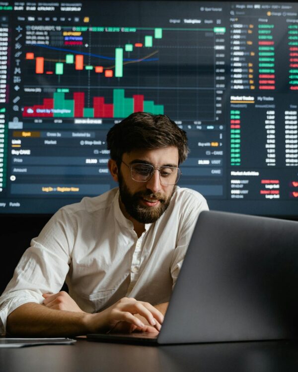 Male analyst studies cryptocurrency trends at a workstation with multiple displays showing market data.