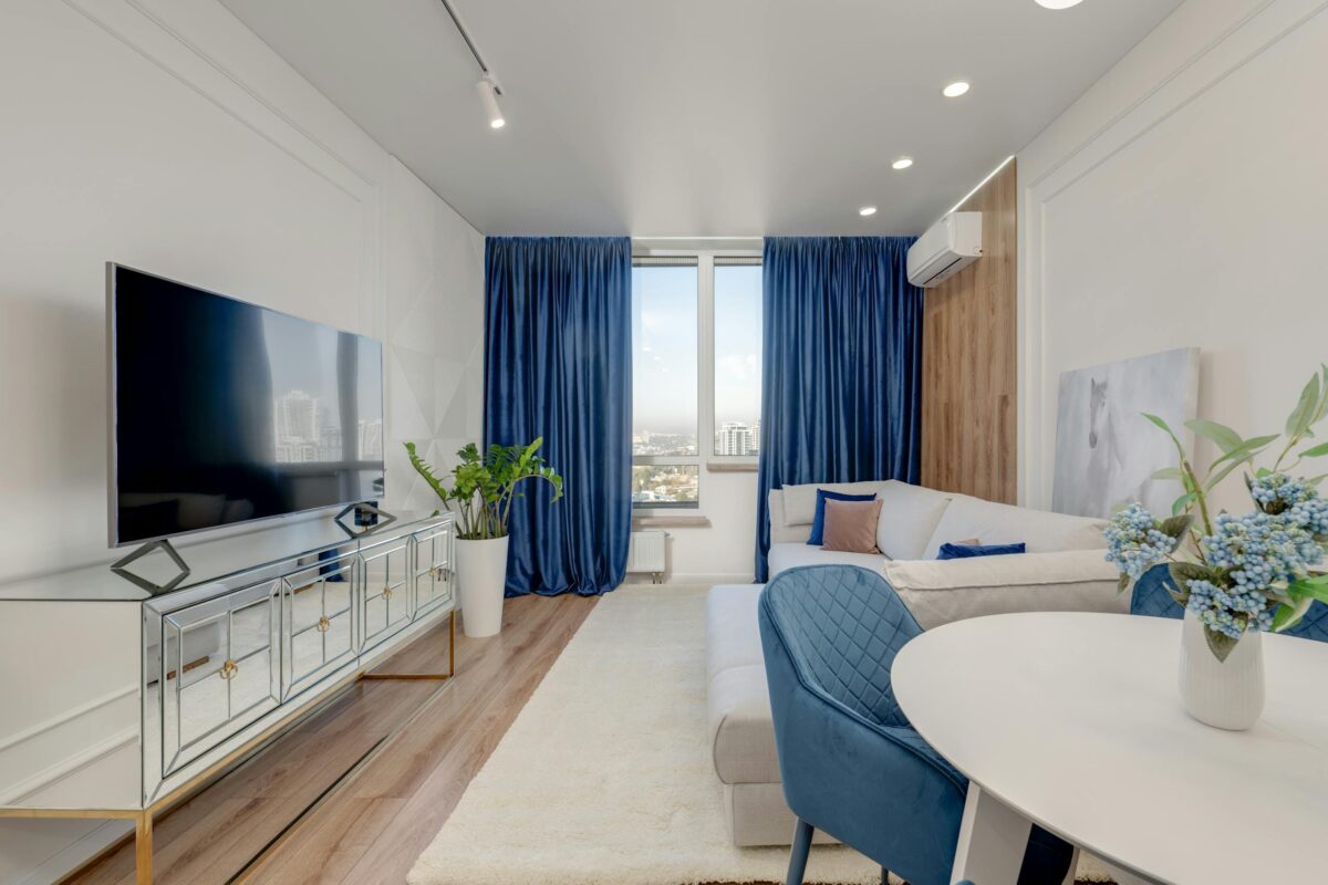 Bright modern living room with a large TV, blue decor, and city view.